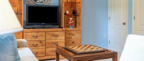 A living room with a television, wooden cabinets, a chess table, and a door.