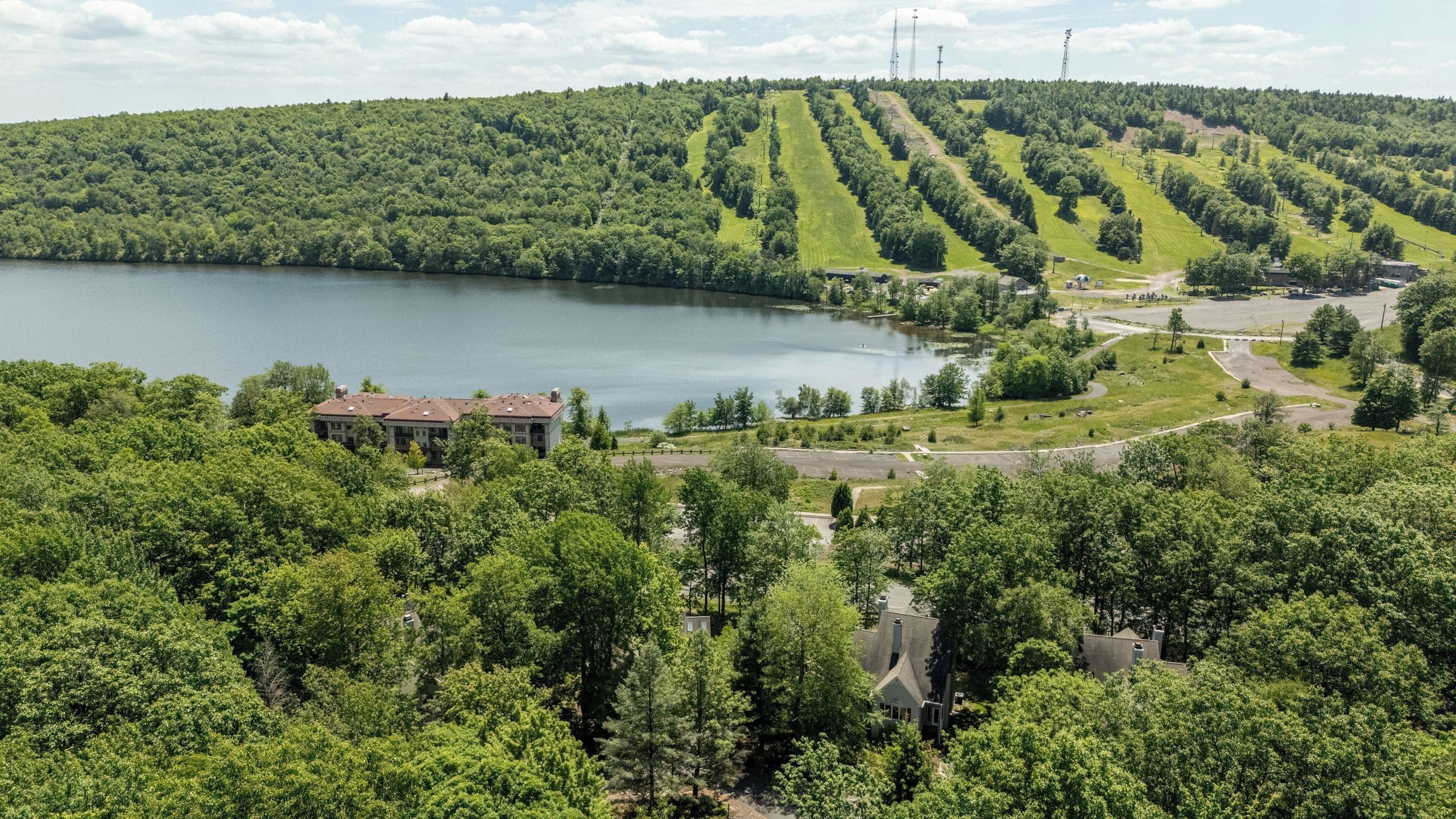 A lakeside property with a large building, a parking area, and a forested landscape.