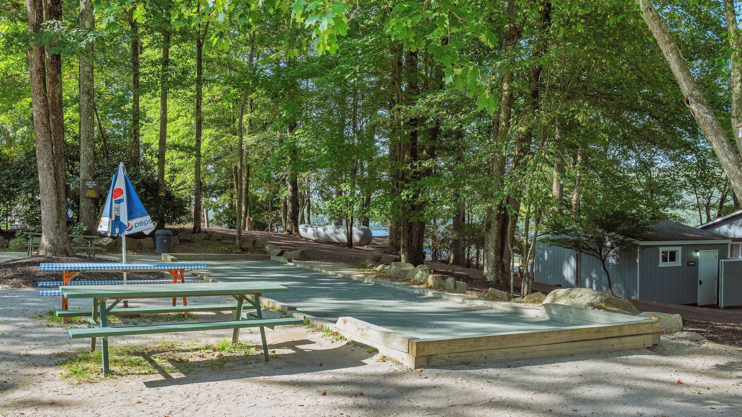 Un camping con mesas de picnic, un paraguas con la marca Pepsi y una cabaña pequeña.