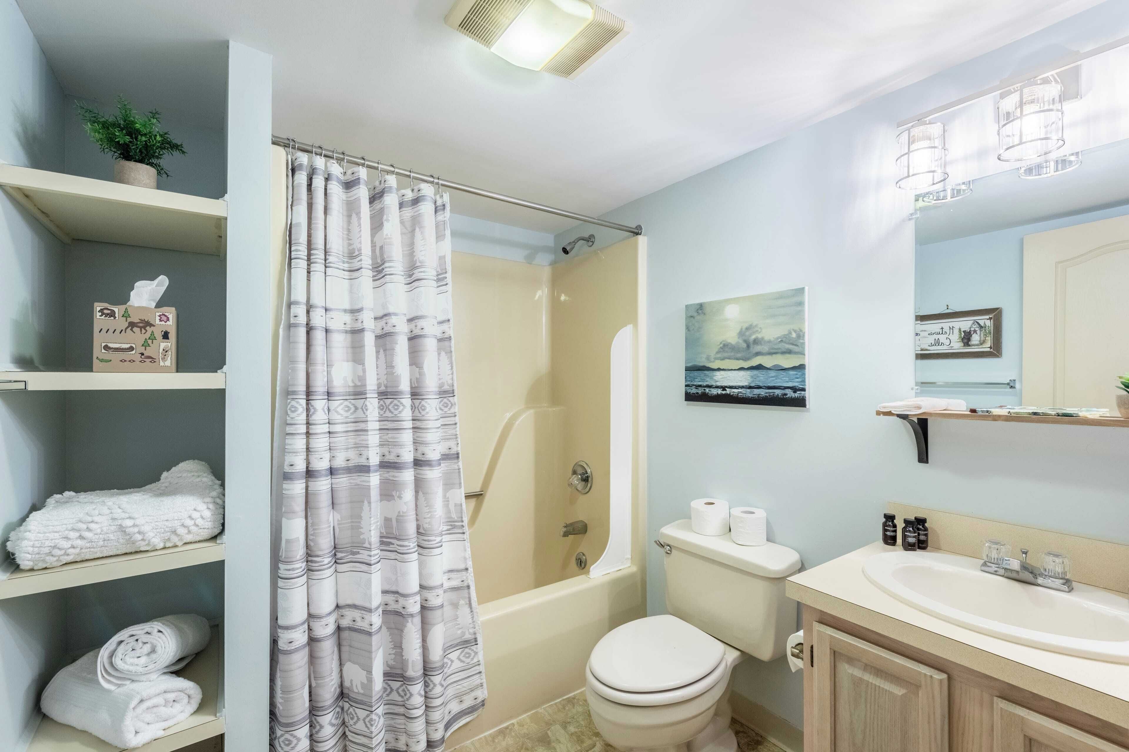 A bathroom with a bathtub, toilet, and sink. There are towels on shelves and a shower curtain.