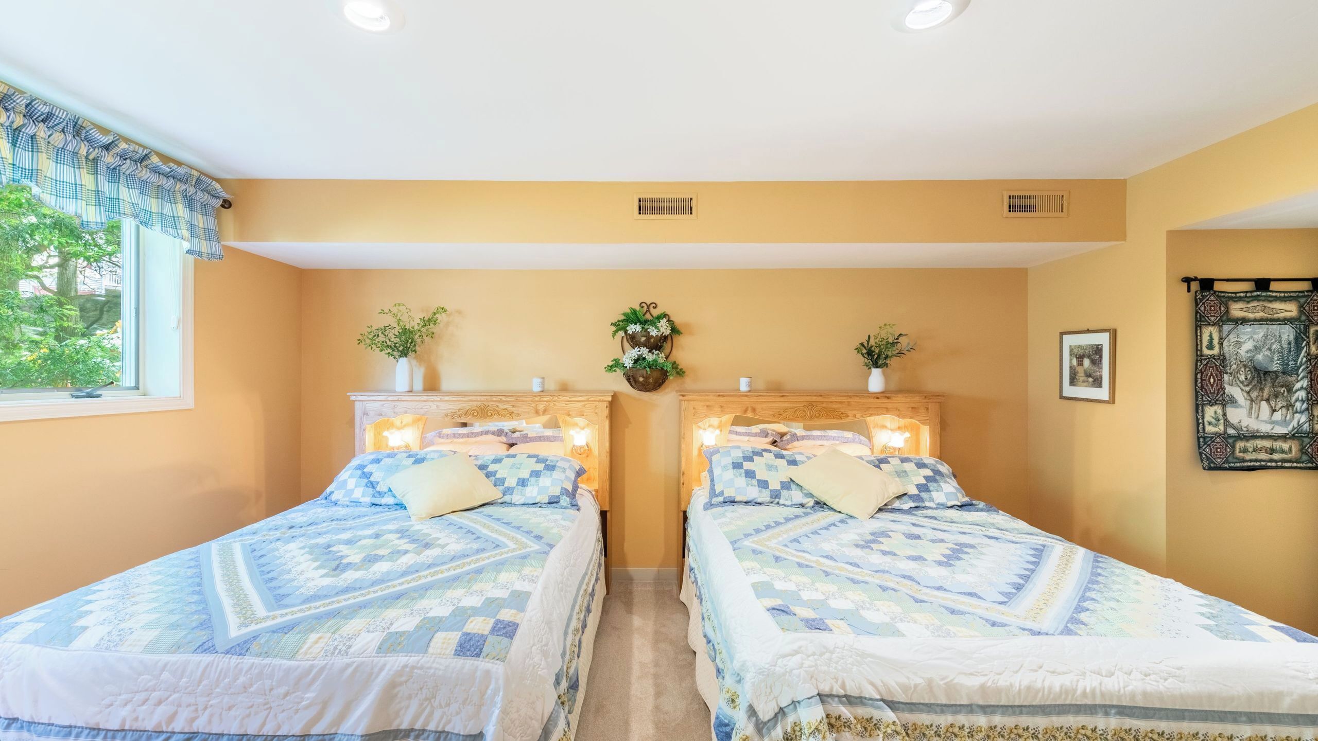 A room with two beds, a window with curtains, a wall-mounted plant, and a picture on the wall.