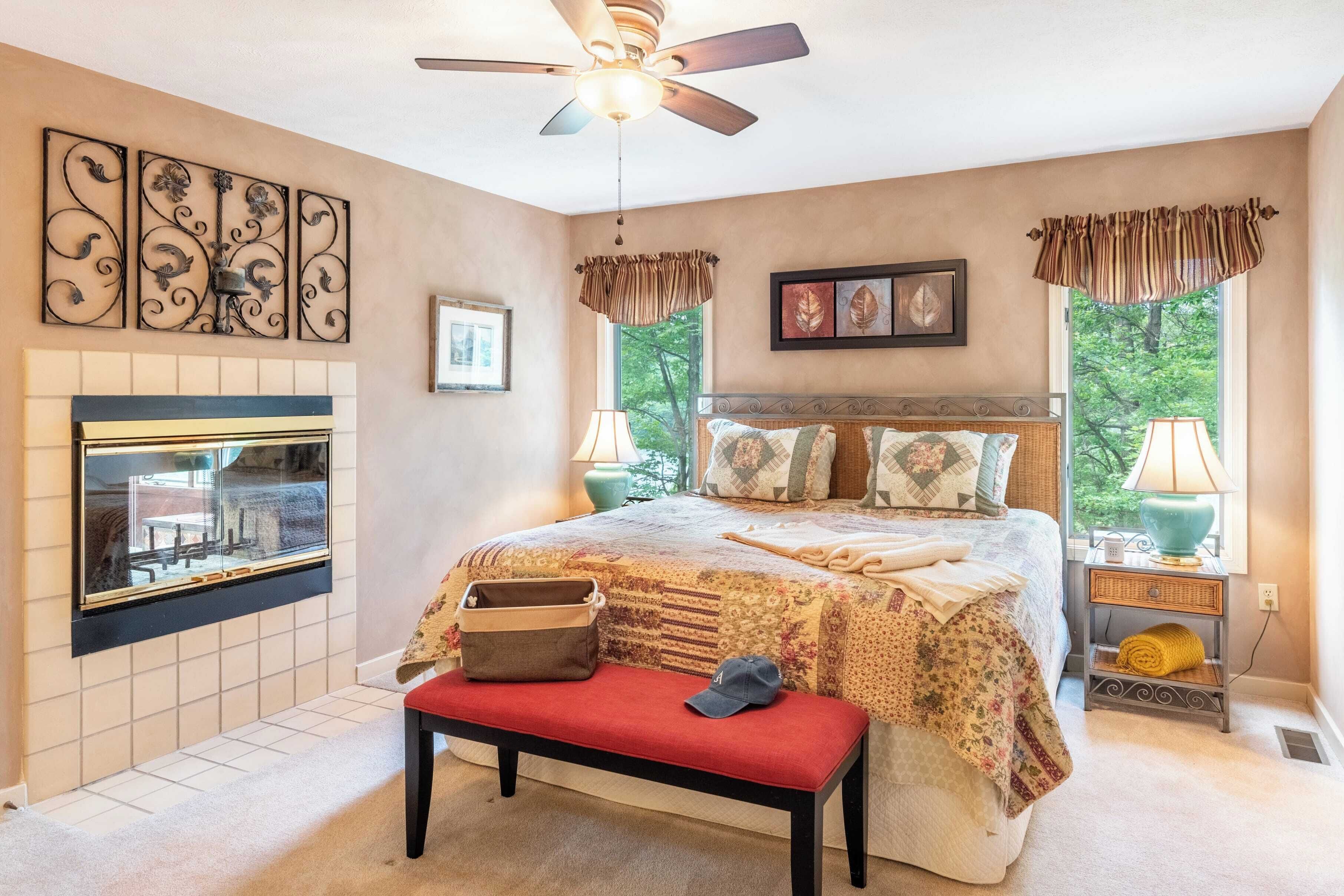 A bedroom with a bed, a bench, a fireplace, and a ceiling fan.