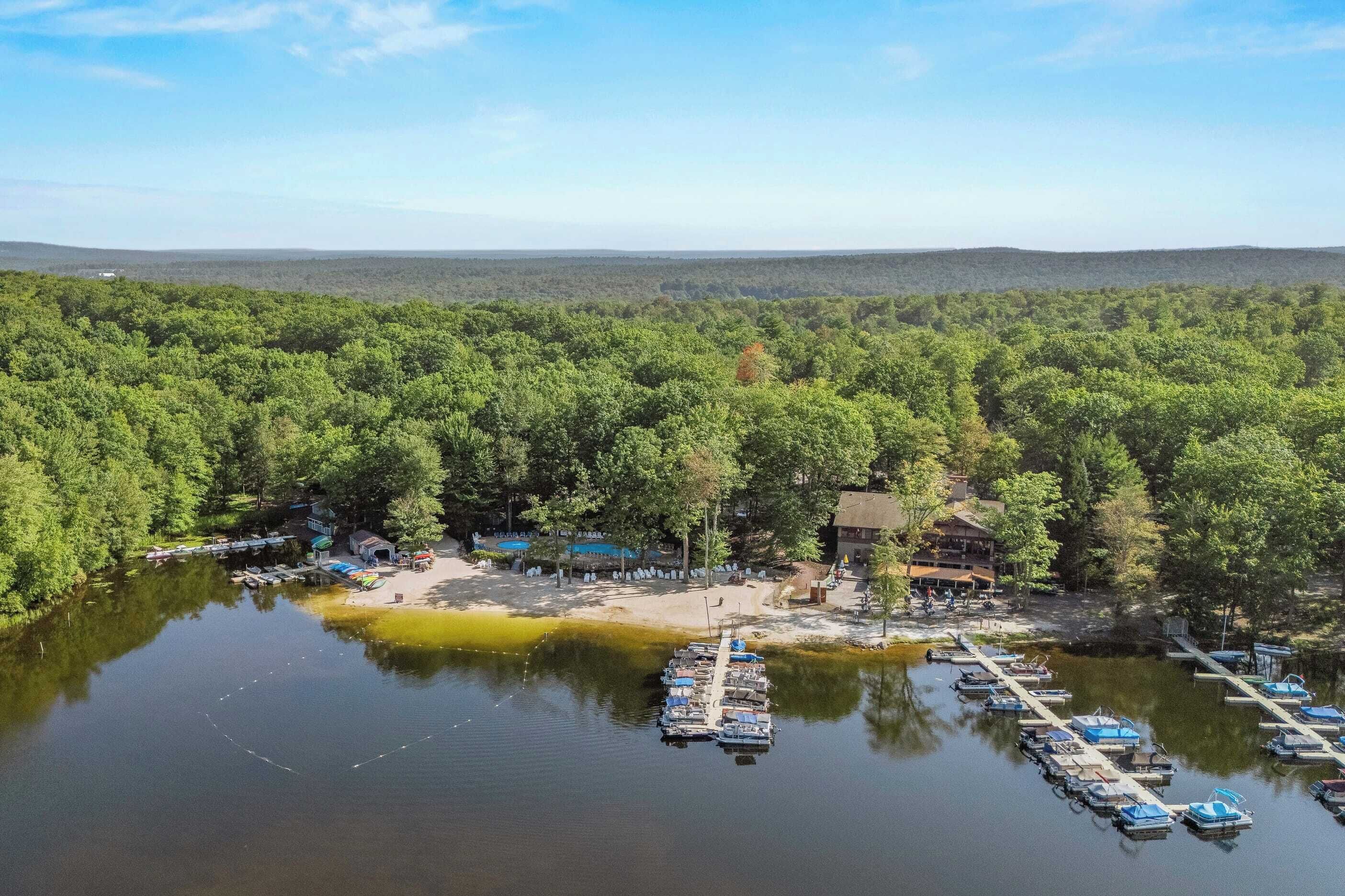 A lakeside property with a dock, boats, and a building surrounded by dense forest.