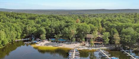 A lakeside property with a dock, boats, and a building surrounded by dense forest.