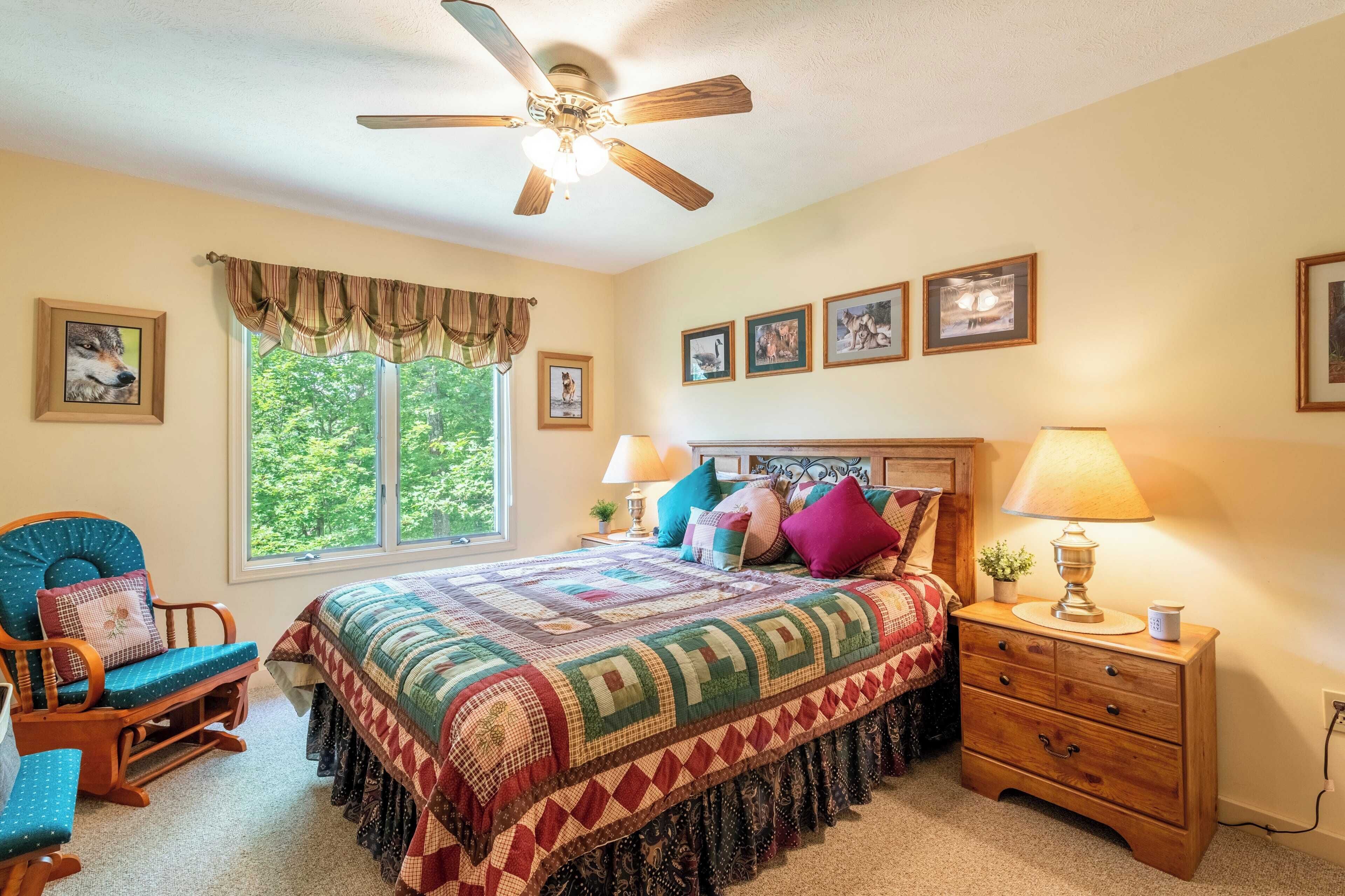A bedroom with a bed, a chair, a nightstand, a lamp, and a ceiling fan.