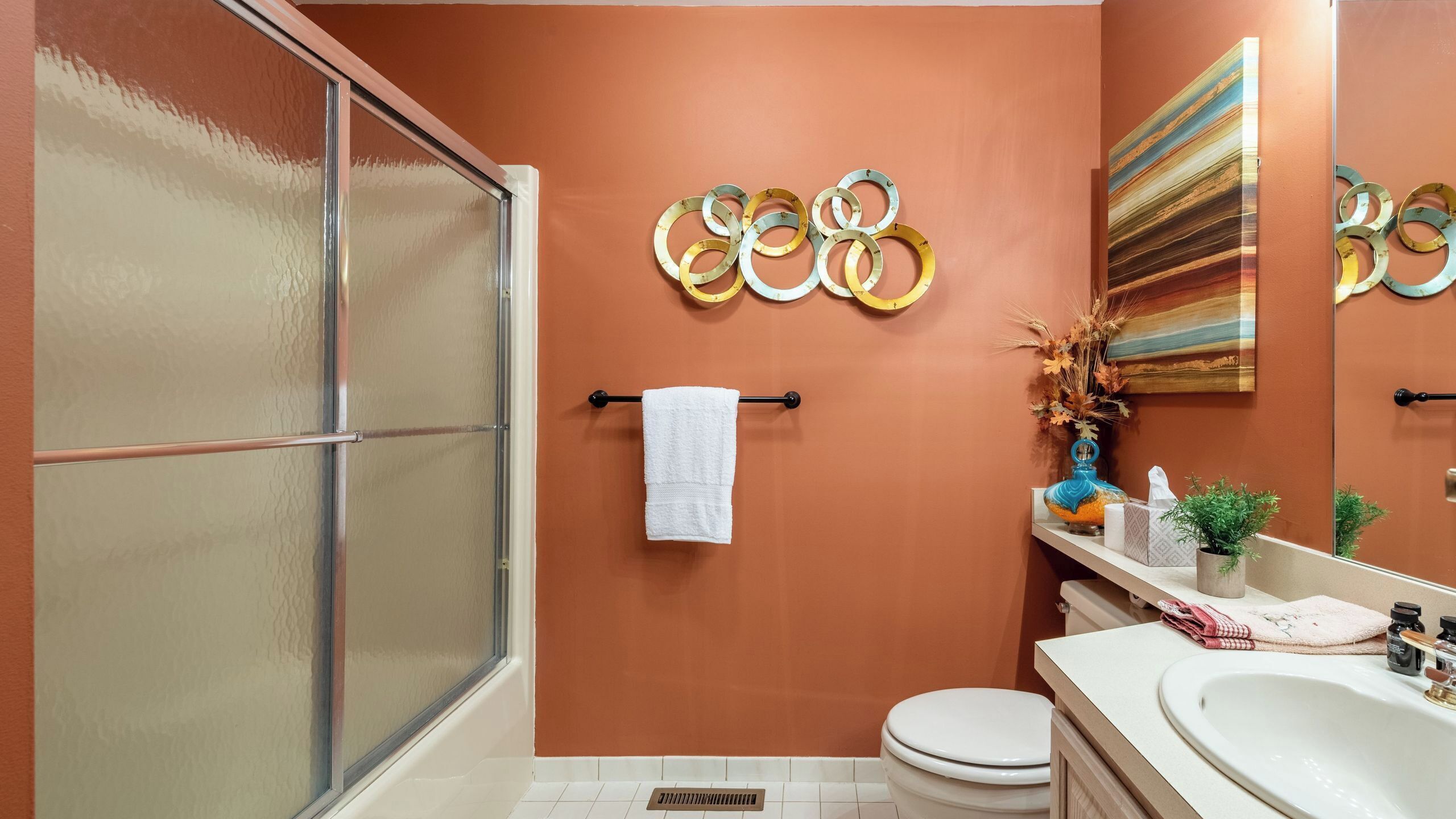 A bathroom with a shower, toilet, sink, and decorative wall art.
