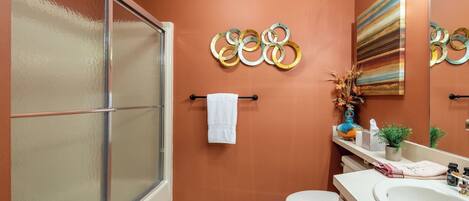 A bathroom with a shower, toilet, sink, and decorative wall art.