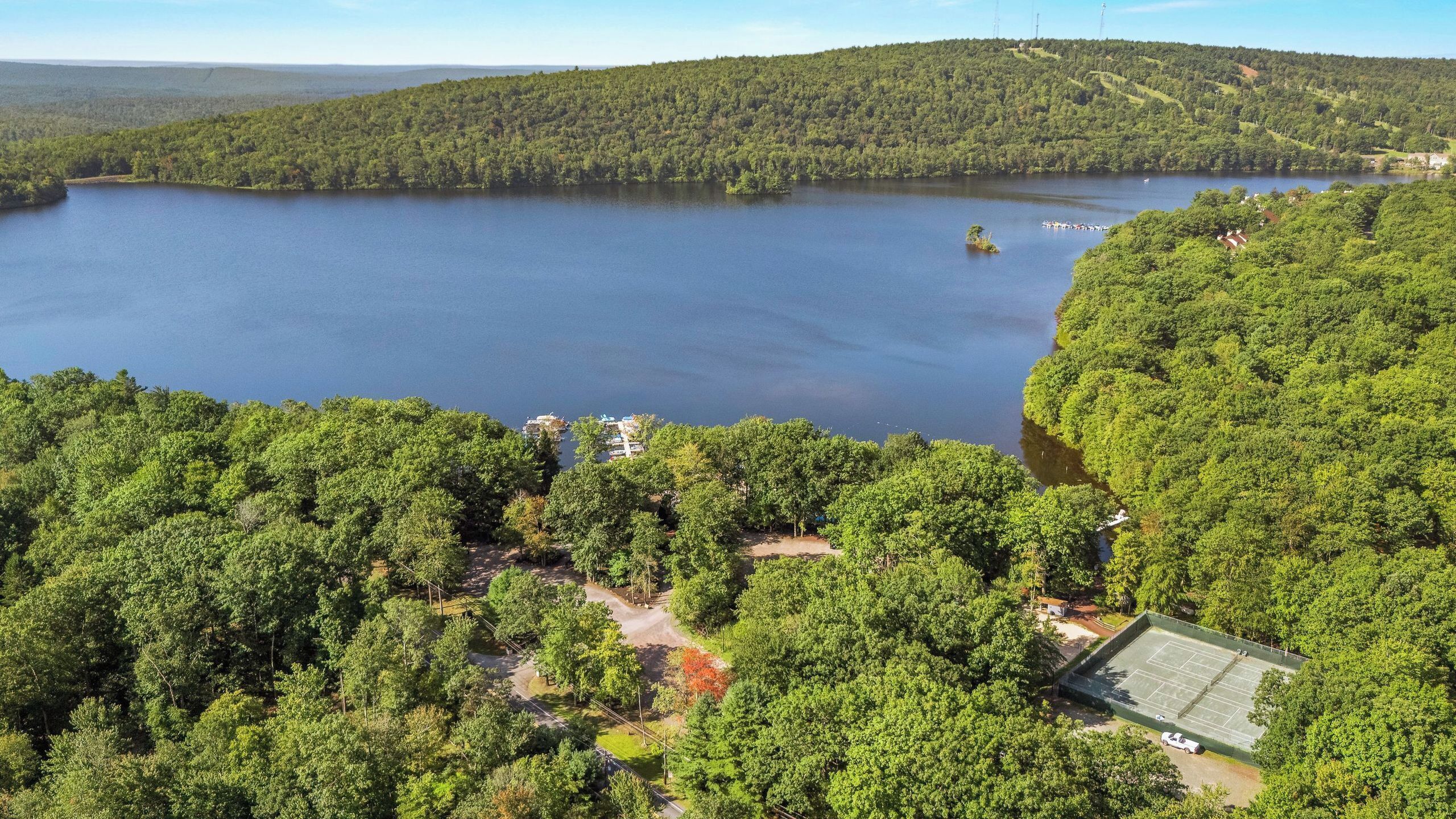 A lake surrounded by dense forest, a tennis court, and a small building.
