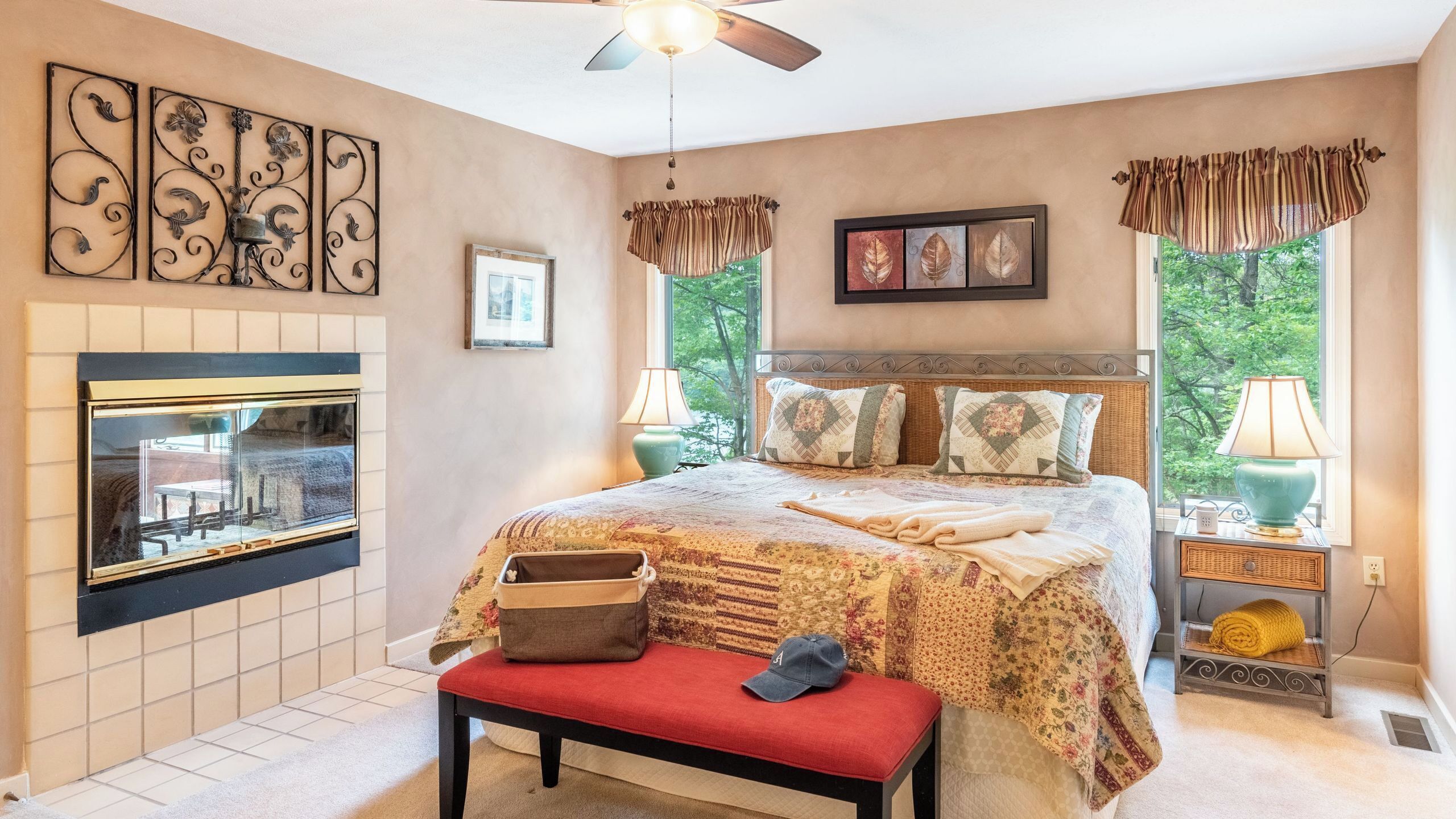A bedroom with a fireplace, a bed with a floral bedspread, a bench, and two bedside lamps.