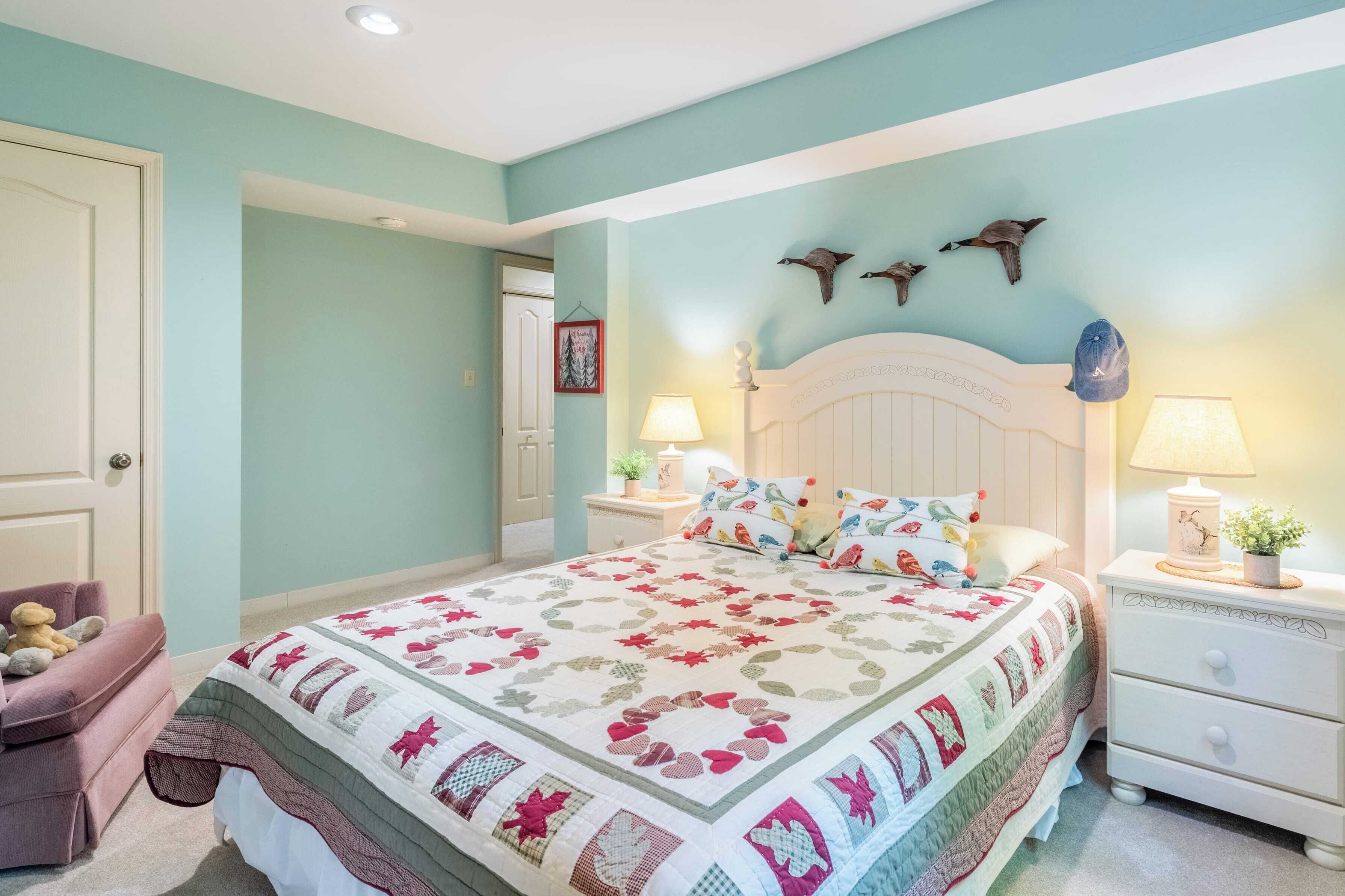 Un dormitorio con cama, mesitas de noche, una silla y adornos en la pared.