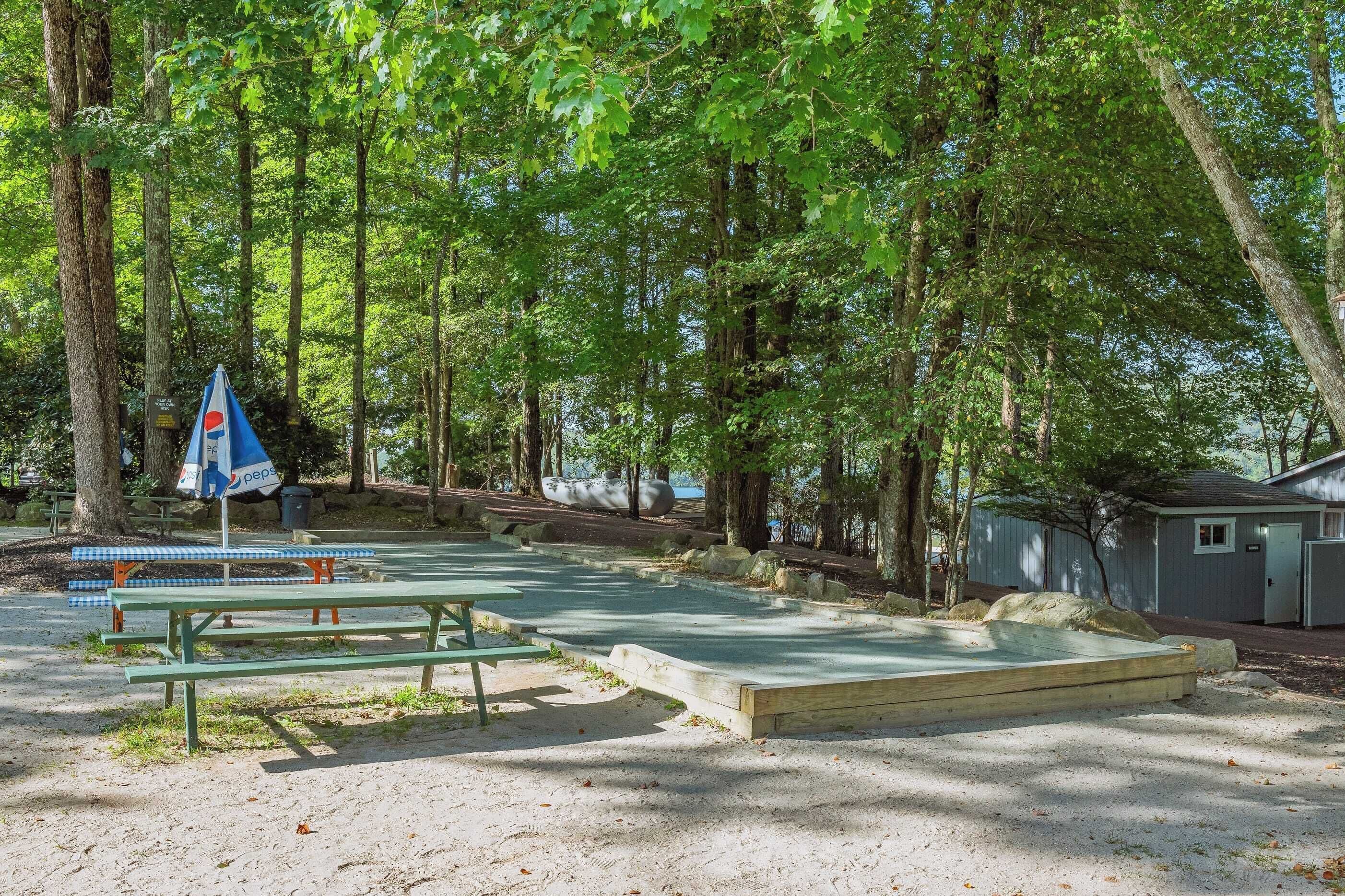 Un área de picnic con bancos y una mesa, rodeada de árboles y un pequeño edificio.