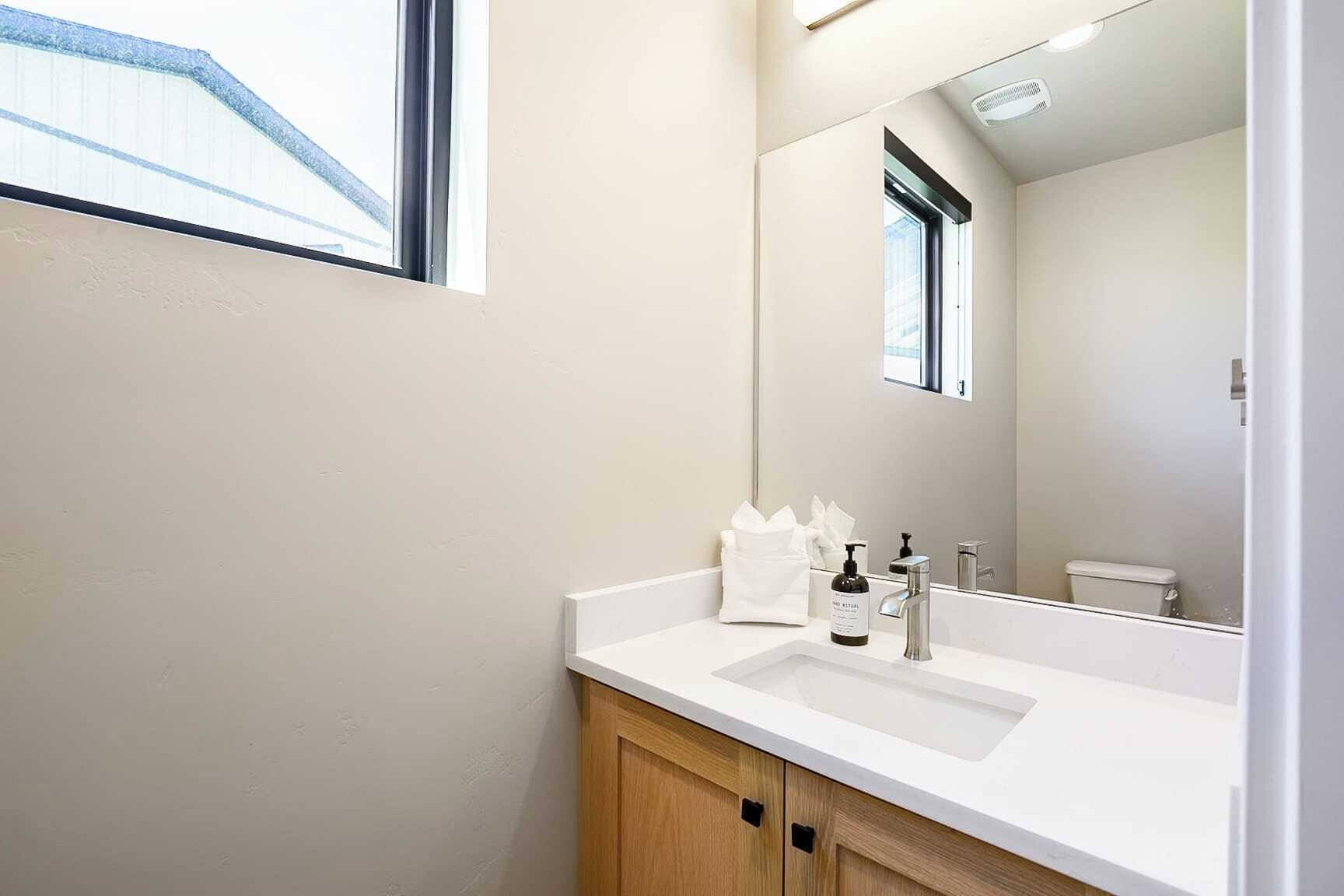 A modern bathroom with a white sink, a large mirror, and a wooden cabinet.