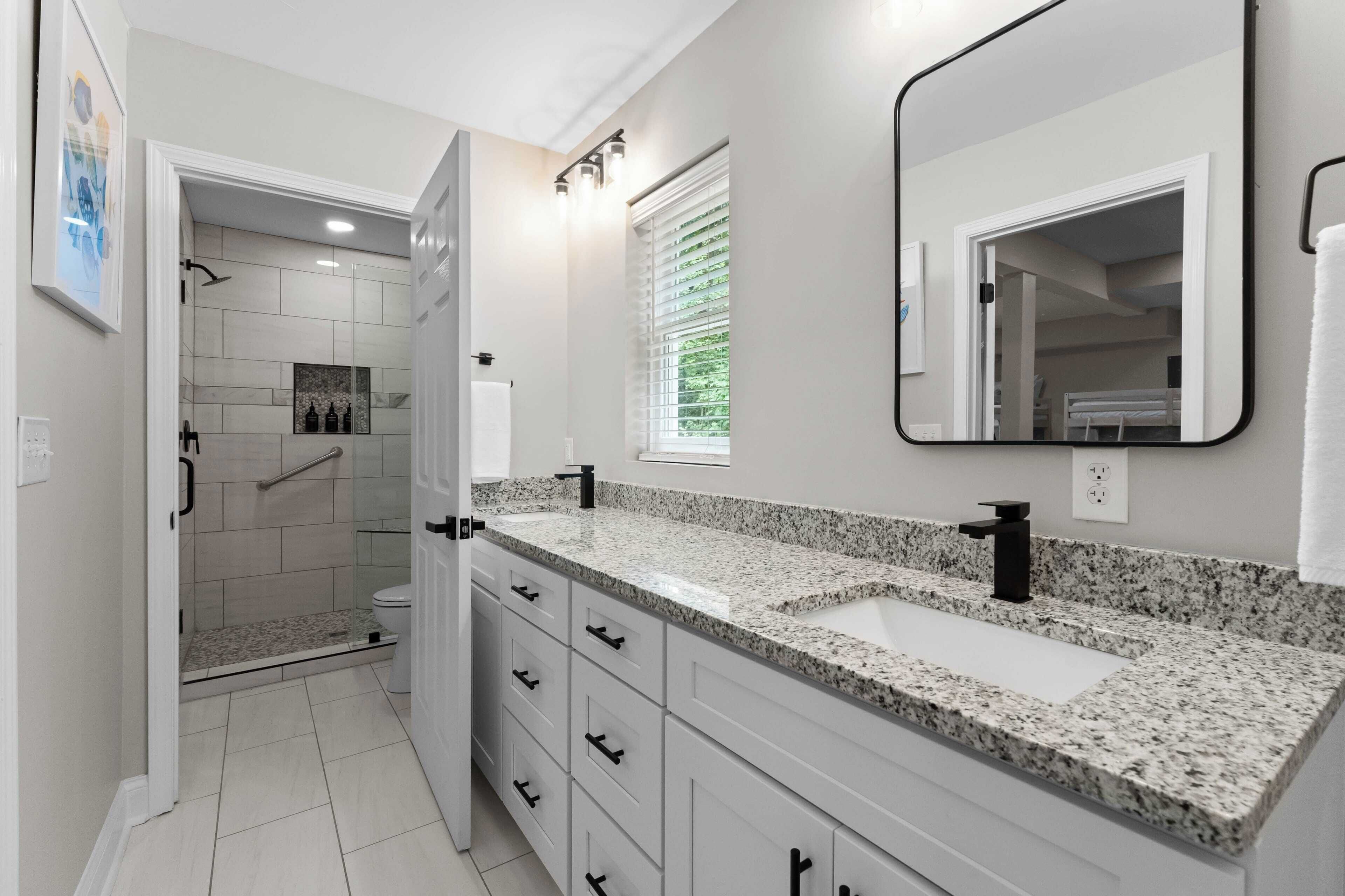 Une salle de bain moderne avec une douche à l’italienne, un grand miroir et un lavabo encastré dans un plan de travail en granit.