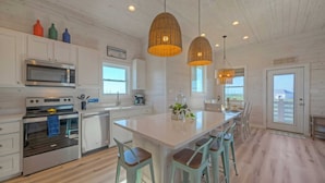 Une cuisine moderne avec des meubles blancs, un îlot central doté de tabourets, un four encastré et des luminaires suspendus.