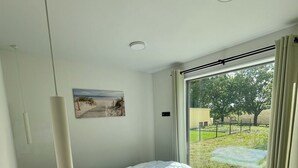 A modern bedroom with a large bed, a ceiling light, a window with curtains, and a painting on the wall. - Where time is lost in the green and relaxation is at home? (Altefähr)