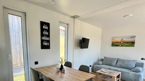 A modern living room with a wooden dining table, grey sofa, and a painting on the wall. - Where time is lost in the green and relaxation is at home? (Altefähr)