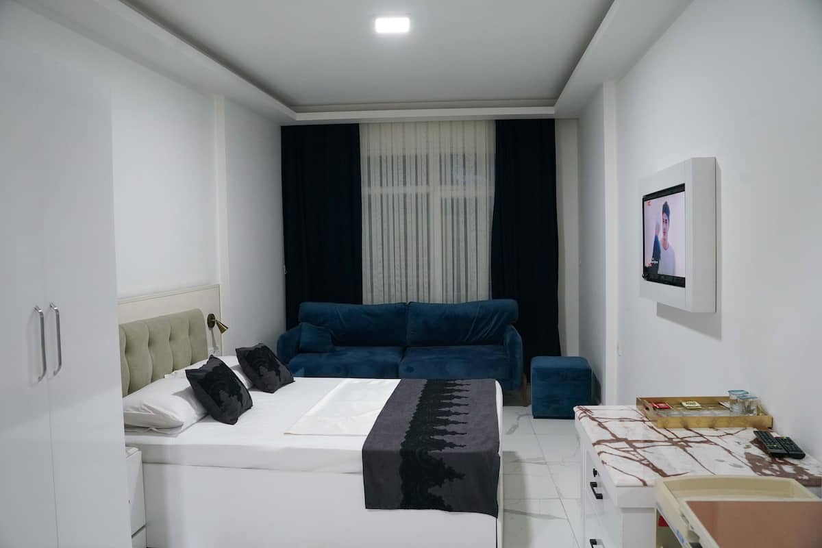 Une chambre à coucher moderne avec un lit, un canapé bleu, une petite table et un téléviseur fixé au mur.