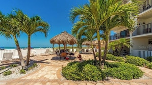 A resort patio with palm trees, a thatched umbrella, and outdoor seating. - Beachside with peekaboo beach view/ heated pool (Madeira Beach)