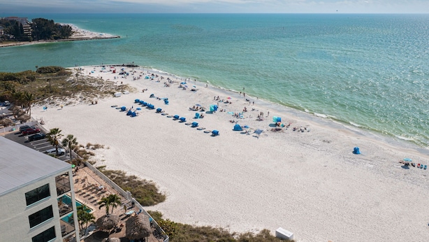 A beach with numerous umbrellas and sun loungers, a clear sky, and a calm sea. - Beachside with peekaboo beach view/ heated pool (Madeira Beach)