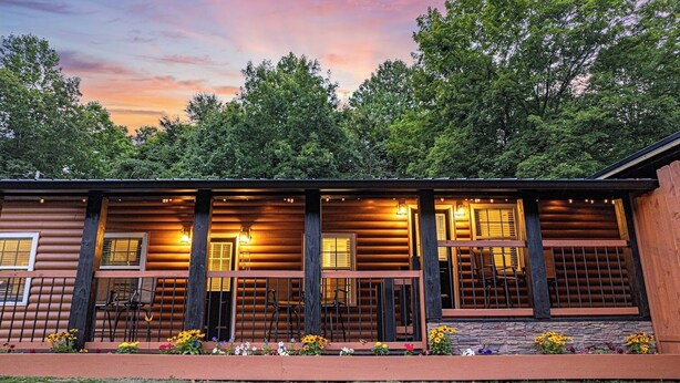A log cabin with a porch, multiple windows, and outdoor lighting.