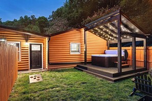 Una cabaña de madera con un patio que incluye un jacuzzi e iluminación colgante.