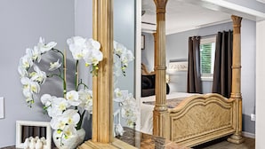 Ein Schlafzimmer mit einem großen Spiegel, einem Bett mit Holzkopfende und weißen Orchideen auf der Ablagefläche.