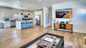 A modern kitchen with white cabinets, a central island with stools, a large refrigerator, and a dining area with a glass table.