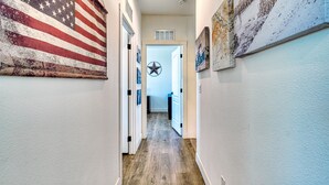 A hallway with a wooden floor, a large American flag on the left, and various framed pictures on the walls.