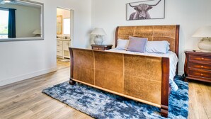 A bedroom with a wooden bed, a large mirror, a bathroom with a sink and mirror, and a bull-themed artwork on the wall.