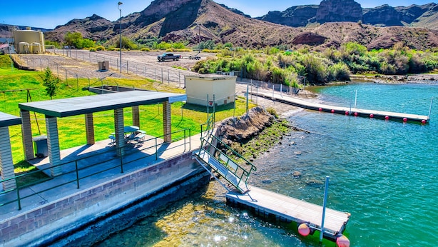 A riverside park with a wooden dock, picnic tables, and a small shelter.