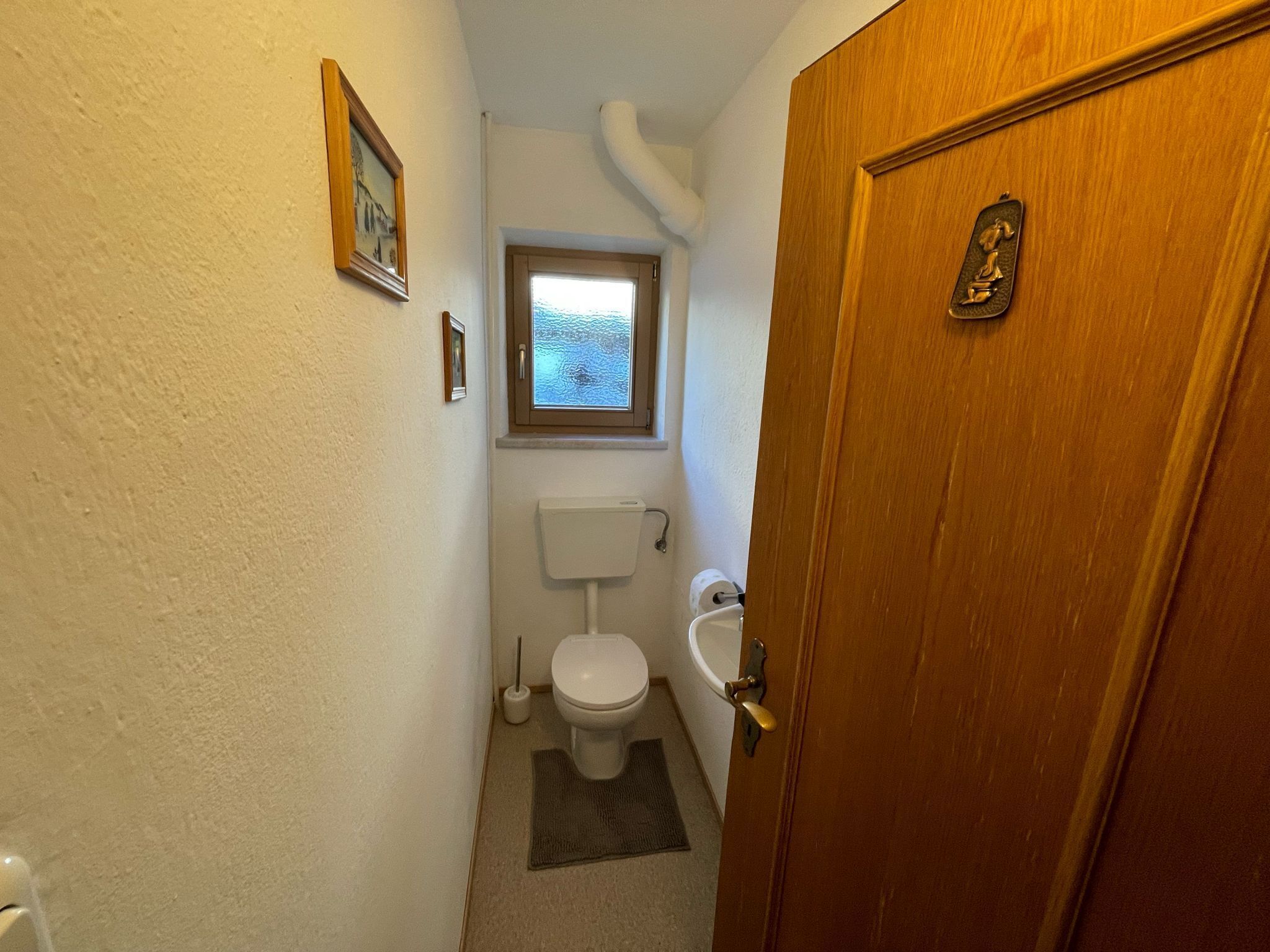 A small, narrow bathroom with a toilet, sink, and window.