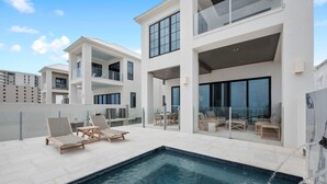 Um edifício residencial moderno com área de piscina no terraço, incluindo espreguiçadeiras e um espaço de refeições com paredes de vidro.