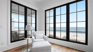 Quarto com grandes janelas de frente para uma praia, sofá, luminária e tapete estampado.