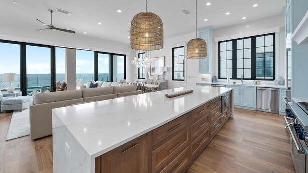 Uma cozinha espaçosa com uma ilha grande, luminárias pendentes modernas e vista para o oceano.