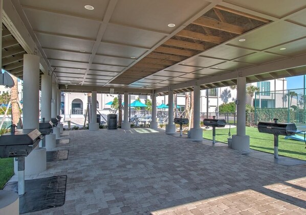 Un espace extérieur couvert, aménagé en patio, avec des sièges, un barbecue et une vue sur une piscine et la verdure.