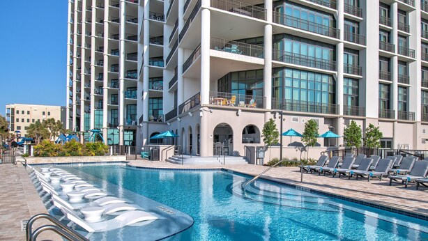 Un hotel moderno con una grande piscina, area relax all'aperto e un edificio a più piani con balconi.