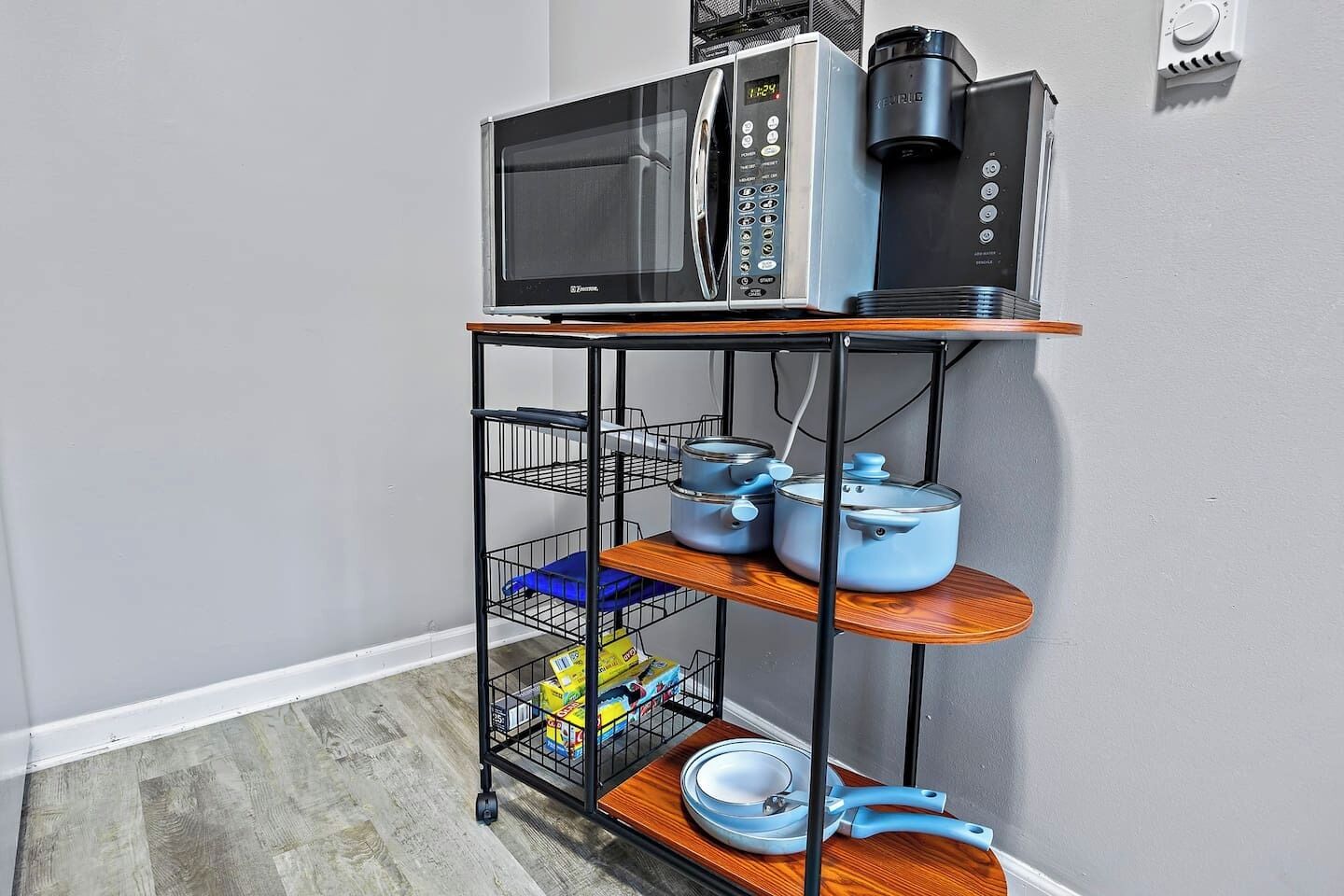 A kitchen area with a microwave, coffee maker, and a shelf holding pots and pans.