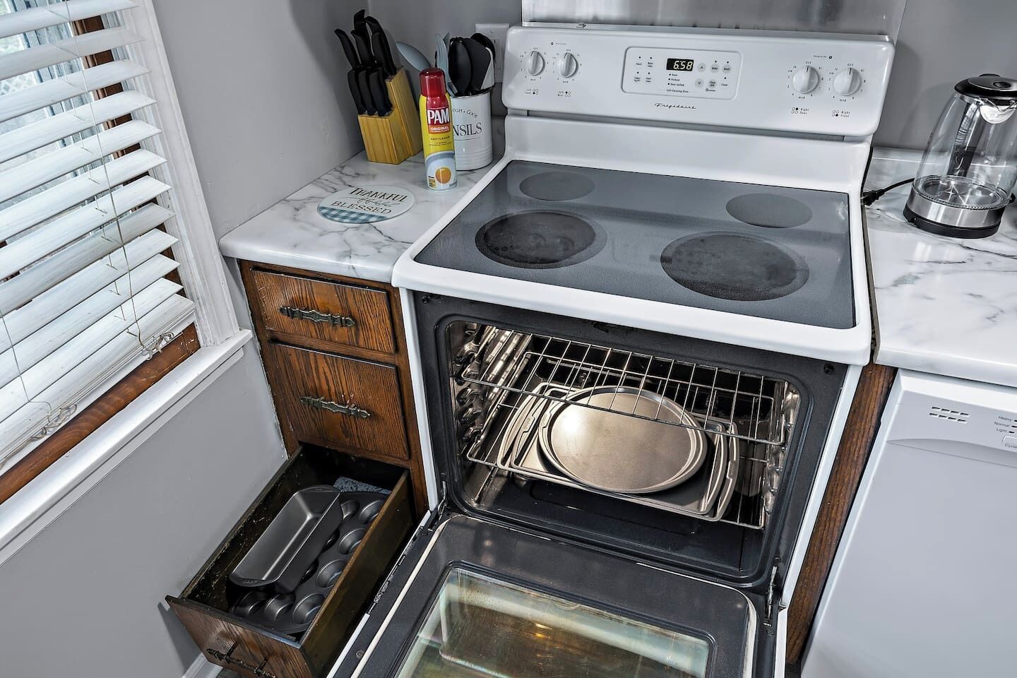 A kitchen with a stove, oven, and a window with blinds.