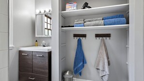 A bathroom with a vanity, a mirror, a shelf with towels, and a trash can. - Relaxing 2BR Riverfront Townhome (Yorkville)