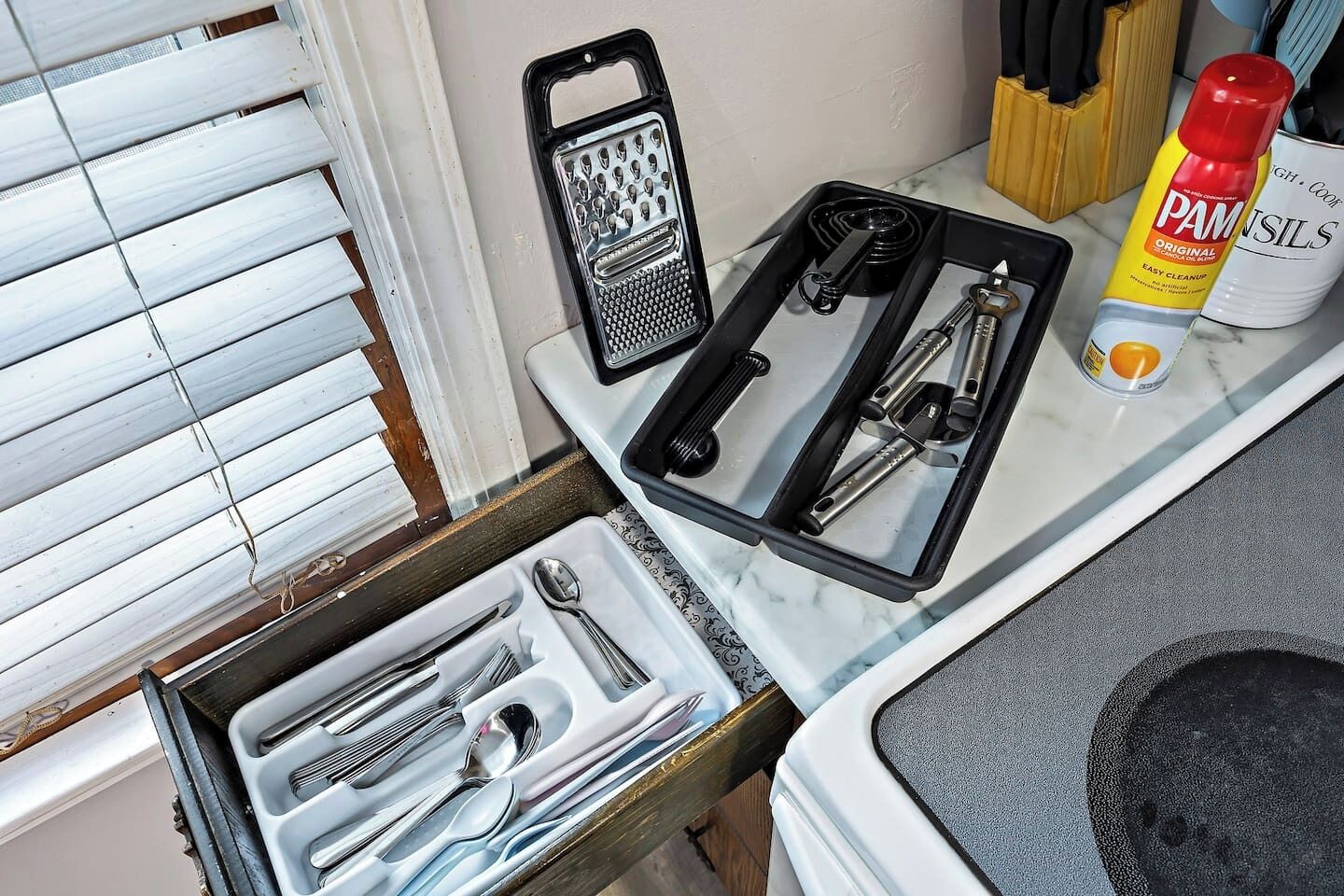 A kitchen counter with a grater, spatula, and a bottle of PAM seasoning.
