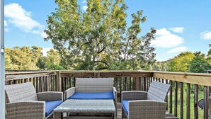 A deck with wicker furniture and a table, surrounded by a wooden railing, overlooking a natural landscape. - Relaxing 2BR Riverfront Townhome (Yorkville)