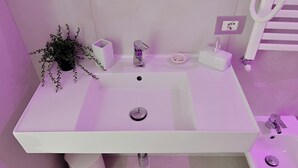 A modern bathroom with a white sink, a small potted plant, and a toilet.