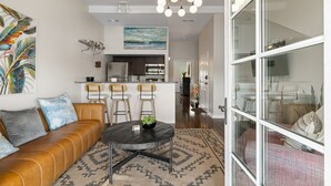 A modern living room with a leather sofa, a round coffee table, and a dining area with bar stools. - Riverwalk Retreat - Downtown water views, parking (Wilmington)