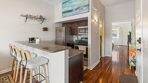 A modern kitchen with a bar area, stainless steel appliances, and a large window overlooking the city. - Riverwalk Retreat - Downtown water views, parking (Wilmington)