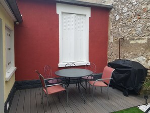 Une terrasse avec une table et des chaises, un barbecue et un mur en pierre.
