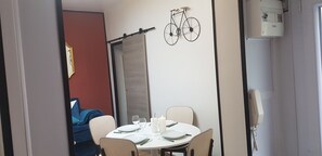 Un coin repas avec une table dressée pour deux personnes, un vélo décoratif fixé au mur et un téléphone mural.