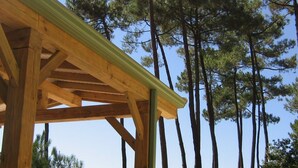 Une structure de pergola en bois offrant une vue dégagée sur de grands pins en arrière-plan.