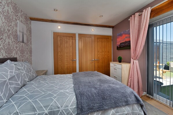 A bedroom with a bed, a dresser, a nightstand, a window with curtains, and a view of the outdoors. - Abbeyview (Whitby)