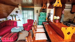 Een knus cabin interieur met houten plafond, rode bank, houten eettafel met bankjes, groene kast en een keuken met spoelbak en kasten.