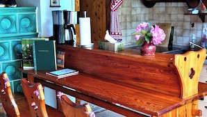 Een houten eettafel met banken, een keuken met een fornuis, en een betegelde vloer.